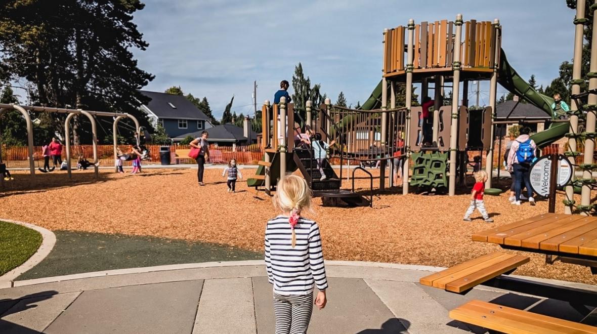A young girl in a striped shirt looks at the new play structure at Loyal Heights Community Center in Seattle's Ballard neigbhorhood among best new playgrounds opened in 2021
