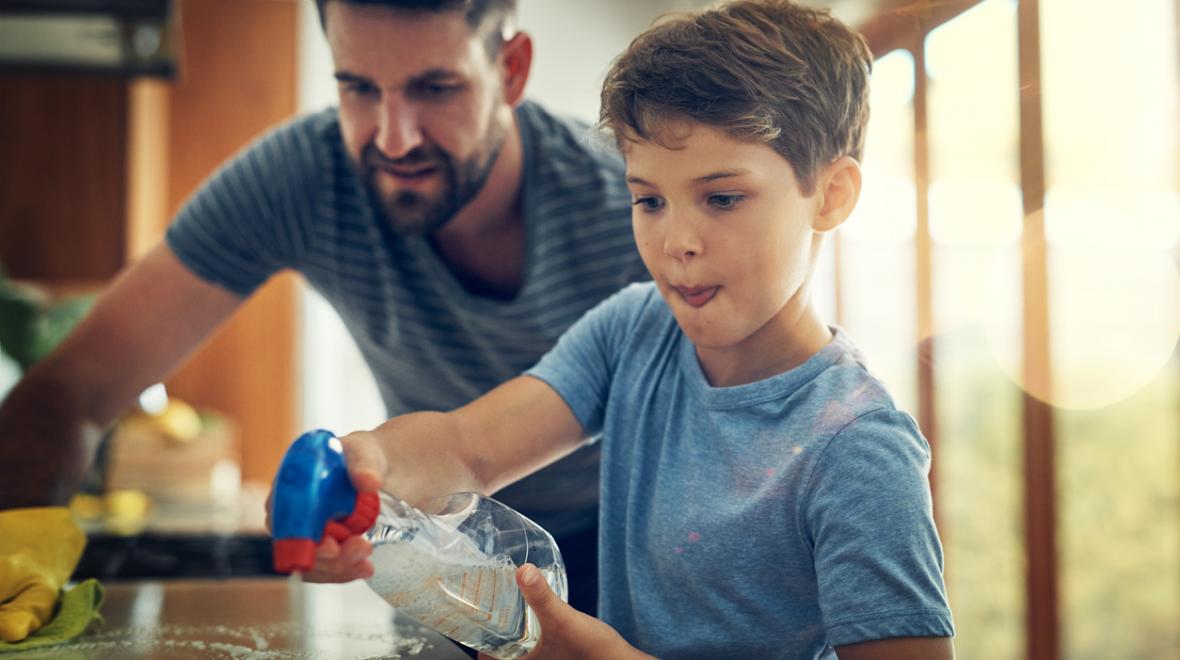 A young boy helps his father clean up the kitchen countertop