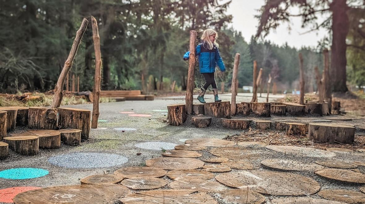 A young girl in a blue jacket plays on the nature features at updated Swan Creek park in Tacoma Washington fun for kids families