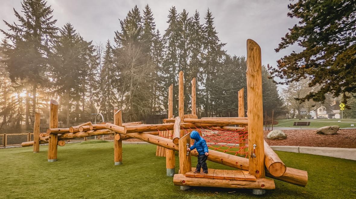 A small boy plays on wooden log play structures at new playground at Westside Park in Redmond, Washington, near Seattle