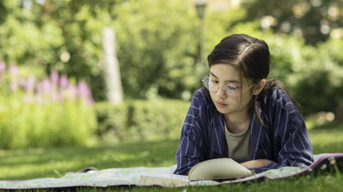 Middle-school-age girl reading a book outdoors in a park