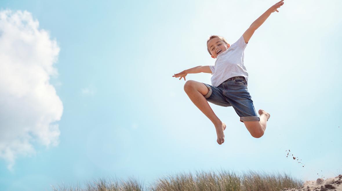 Adorable boy wearing shorts leaps into the air on a sunny day