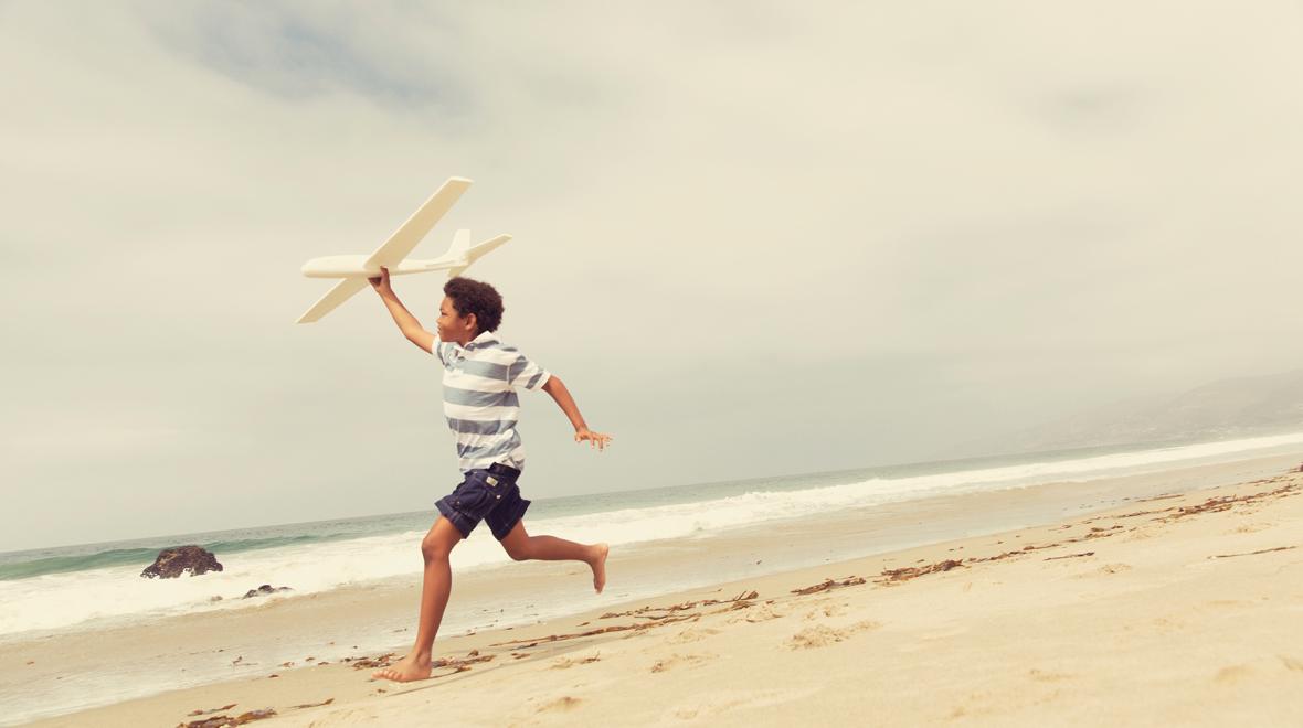 Young boy flies a toy glider plane on a beach