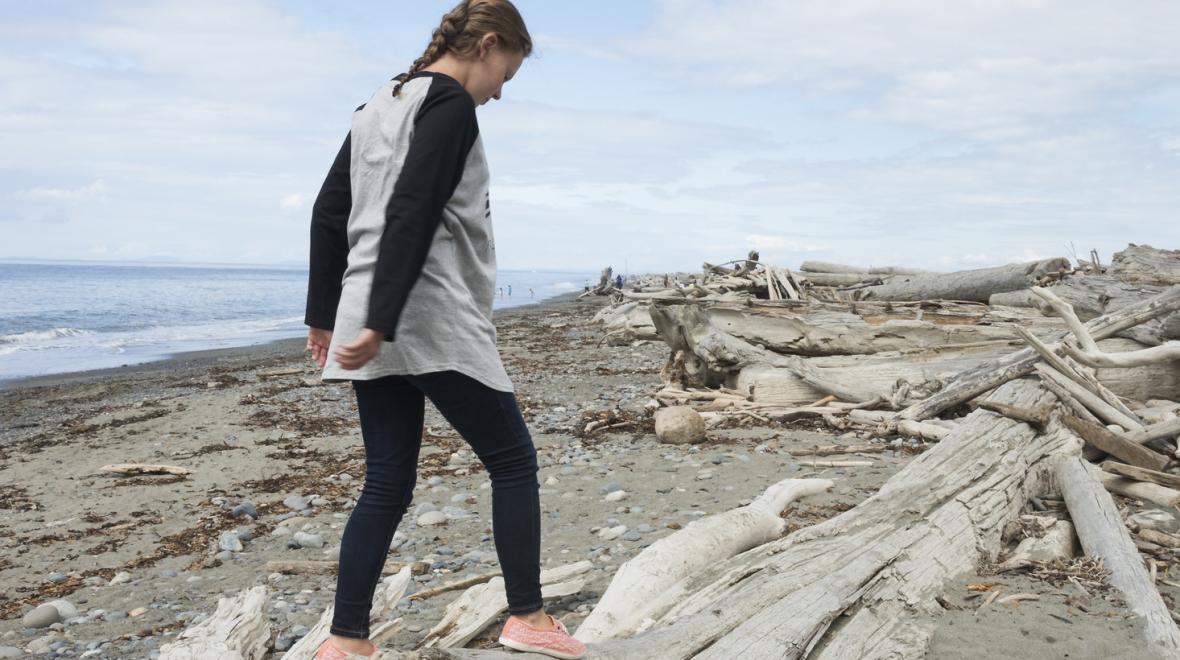 Girl climbing on driftwood along Dungeness Spit Sequim Washington great family road trip itinieraries from Seattle