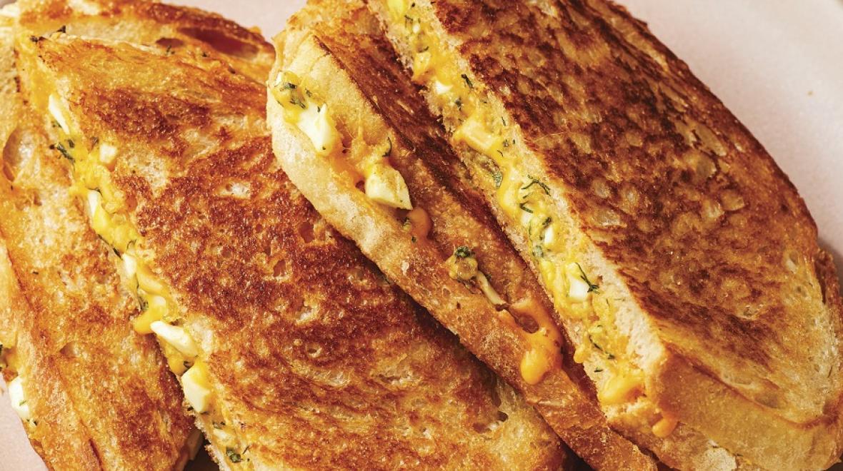 A plate with a toasty, cheesy egg salad sandwich on it