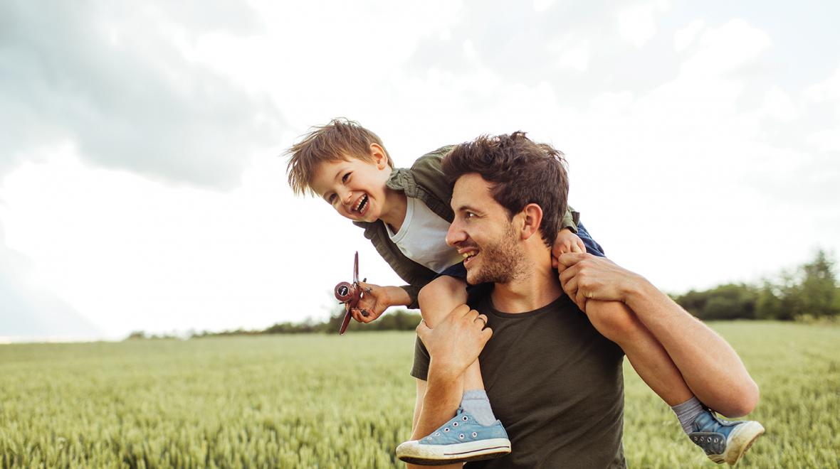 Dad with child on his shoulders in a grass field