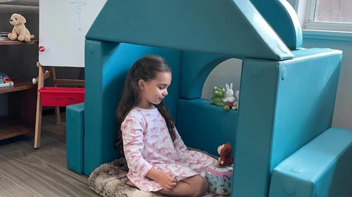 Young girl sitting in a FORT smiling with a toy