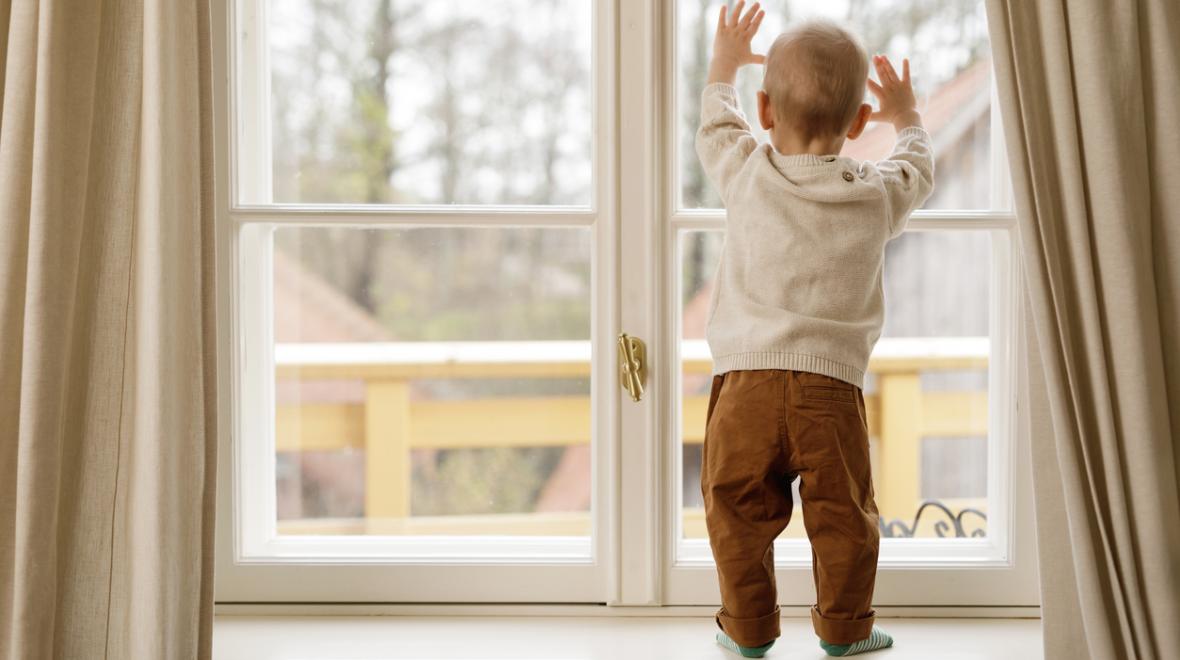 Child standing on a window ledge looking out 