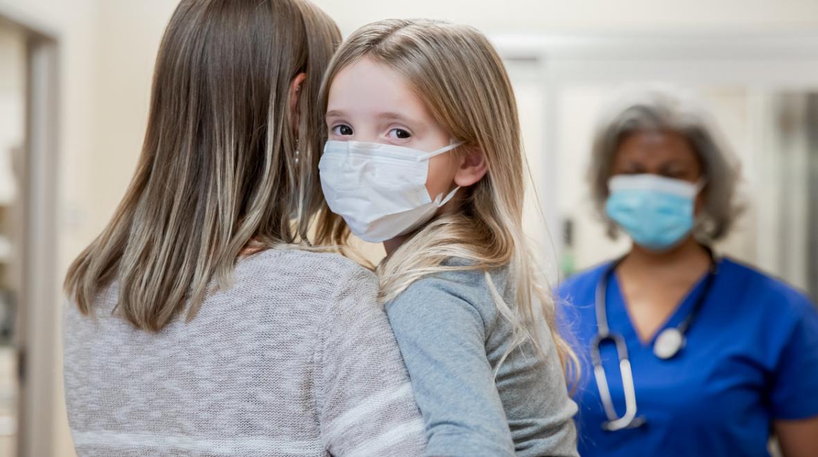 Mom holding young girl wearing mask in a hospital