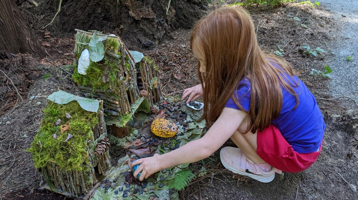Young girl crouches next to a fairy house along the Pine Lake Fairy Trail in Sammamish, Wash., near Seattle, among fun free kids' activities for summer 2022