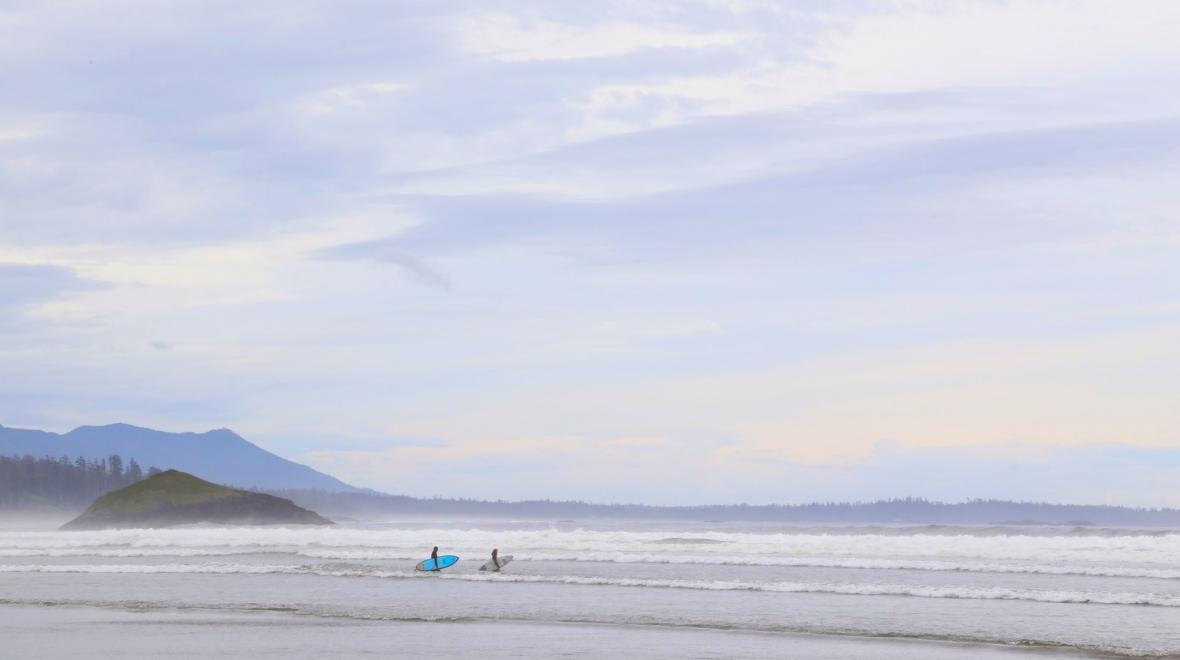 Two surfers walking on the beach in Tofino, B.C., a nearby pacific northwest road trip destination for seattle families