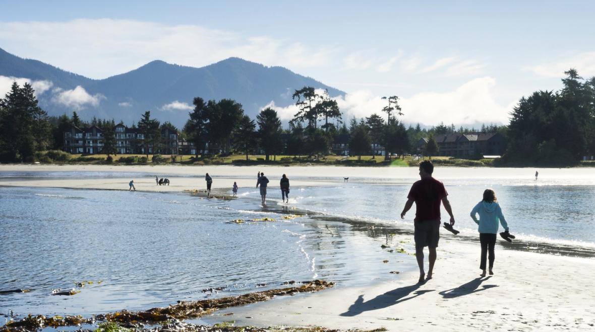 A parent and child walk on a sand spit on the beach at Tofino, British Columbia, an amazing road-trip destination for families from Seattle