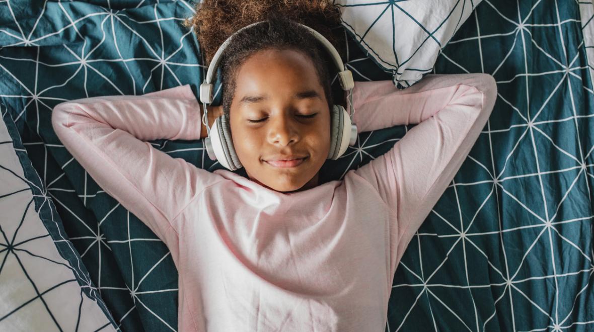 Girl lying in bed with headphones on listening and relaxing 