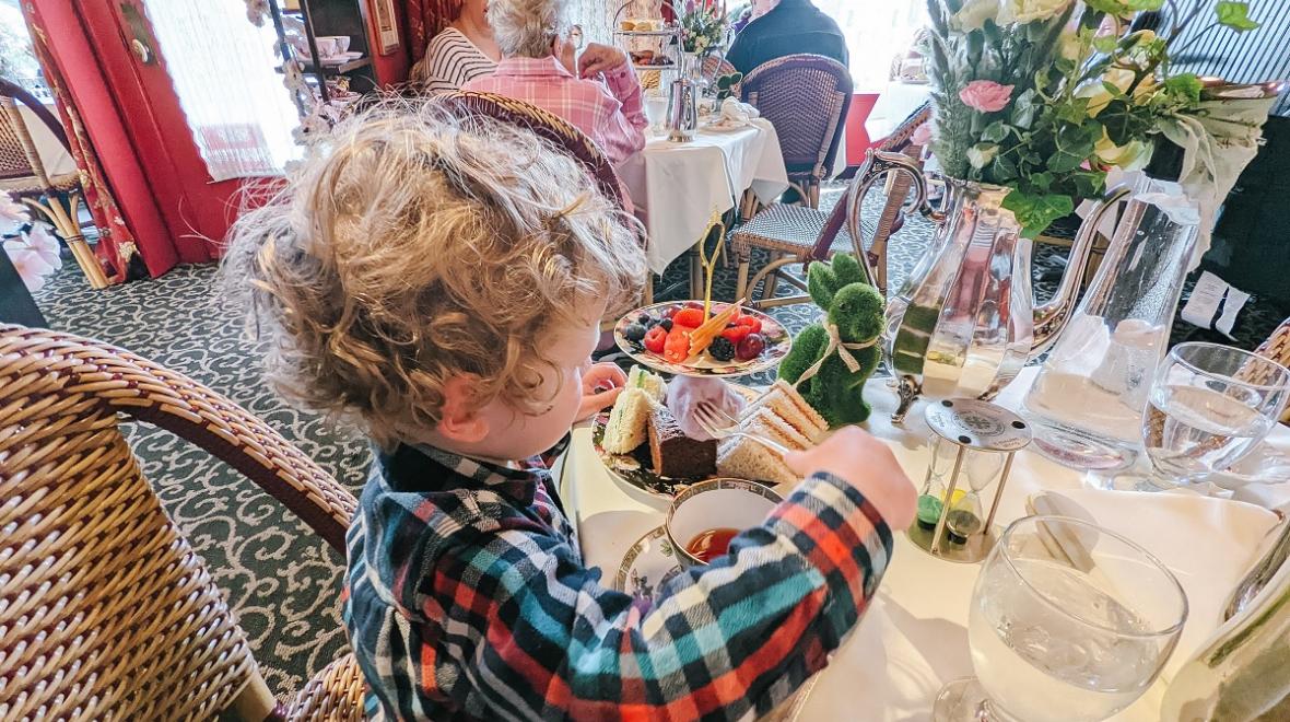 A young boy in a plaid shirt sits at a table and enjoys afternoon tea in Seattle with purple cotton candy, among many treats served to kids at the Queen Mary Tea Room in Seattle