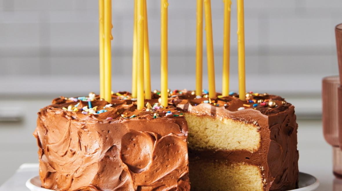 Yellow birthday cake with tall yellow candles and chocolate frosting