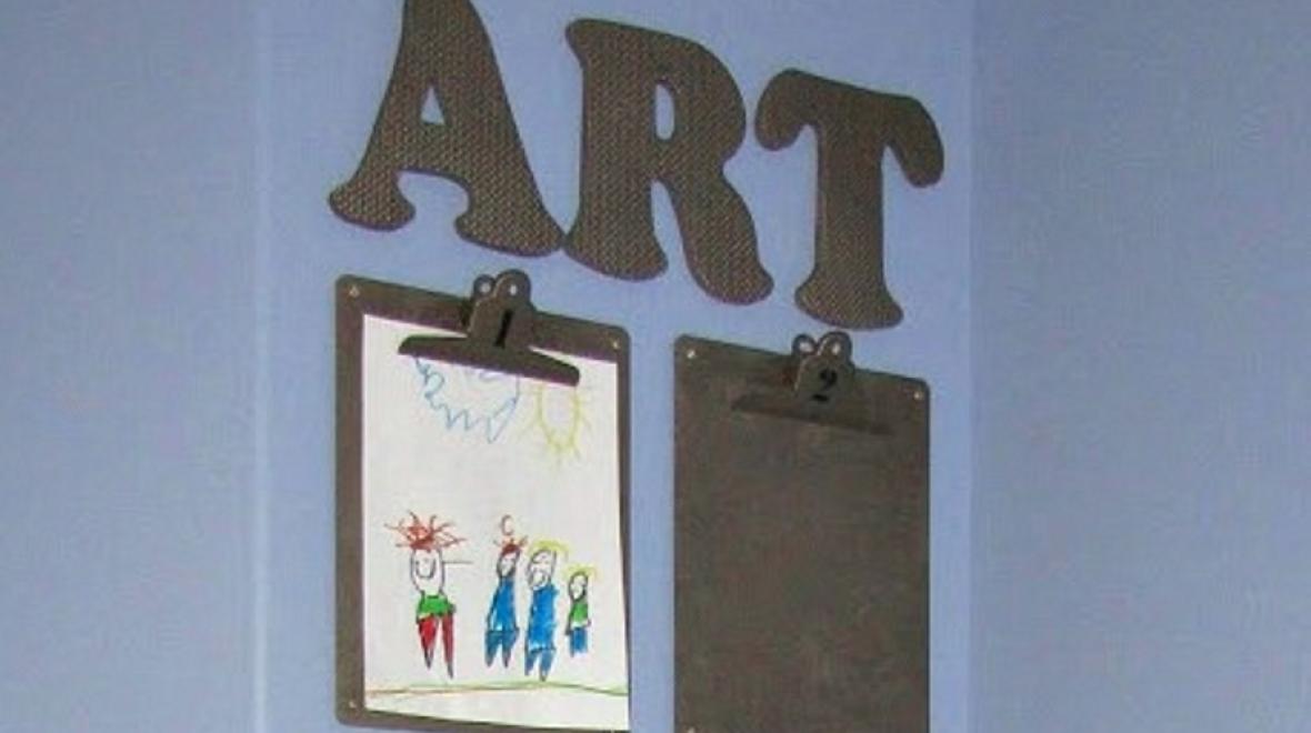 Clipboards hanging on a wall displaying kid art
