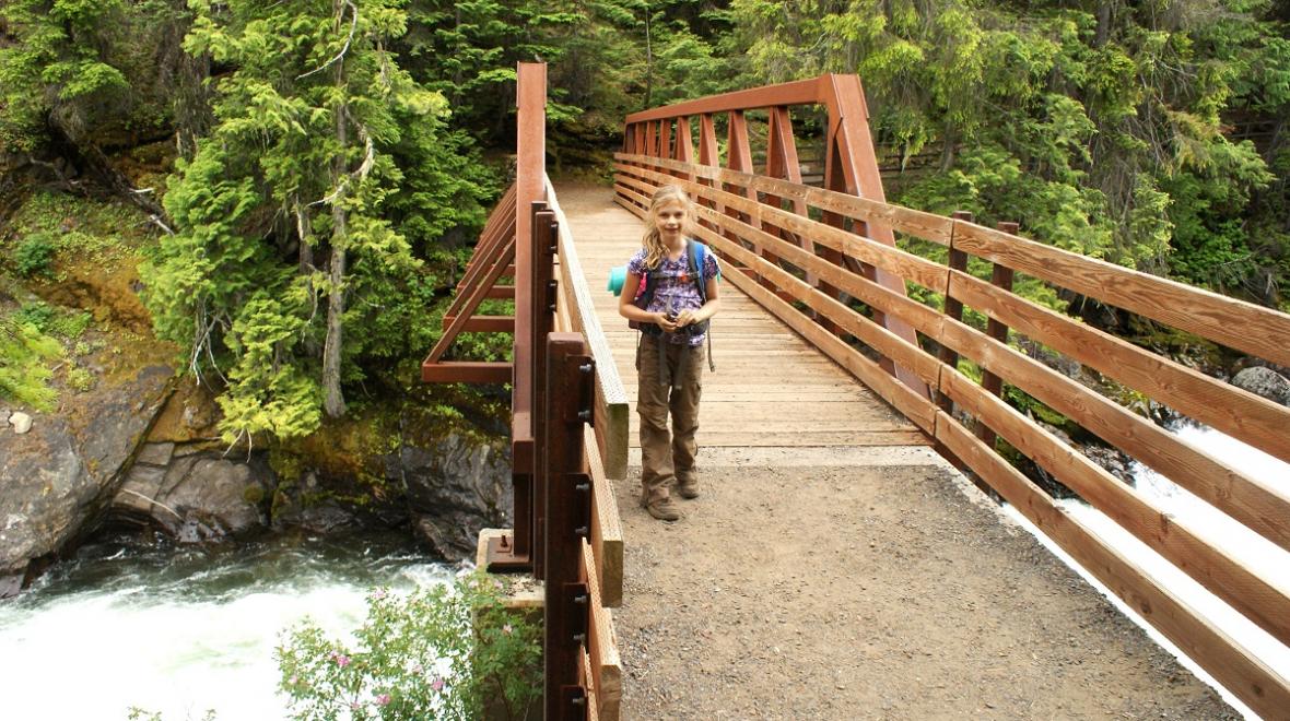 A girl hiker with a backpack poses on a footbridge across the Icicle Gorge near Leavenworth, among best wildflower hikes for families