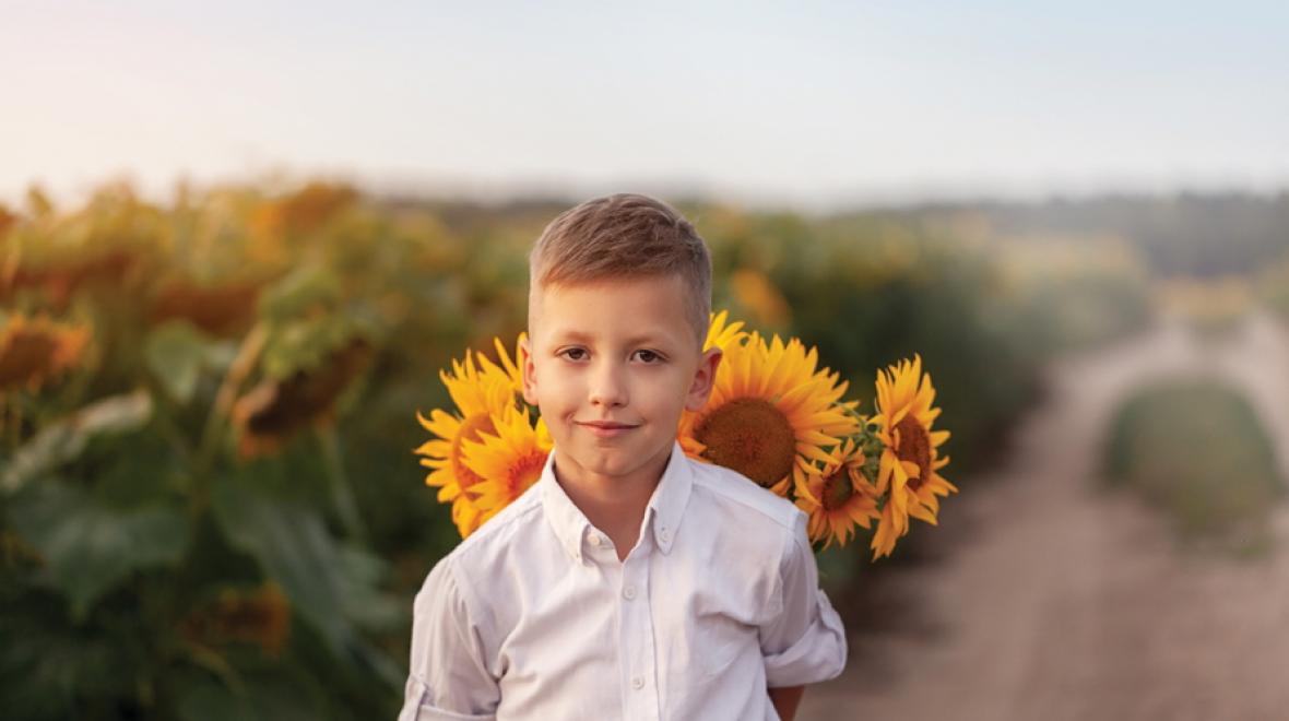 Little boy standing in front of a sunflower in a field