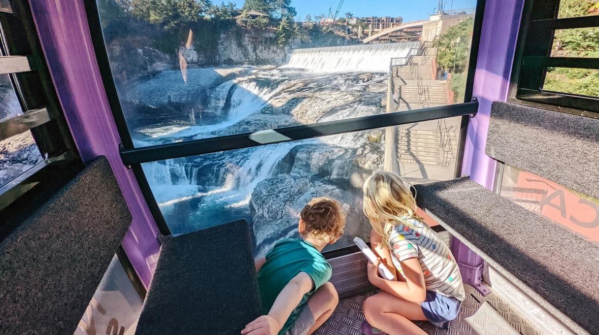 Two children looking through a window at Spokane Falls from the Numerica Sky Ride over the Spokane River