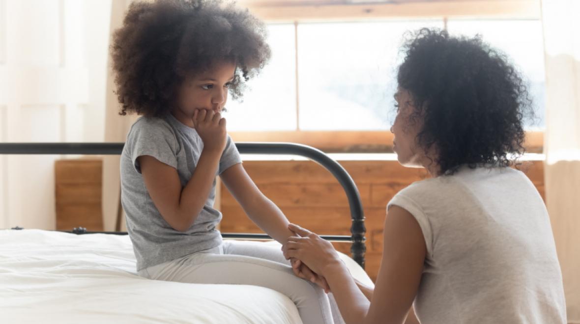 Young girl looking shy and sitting on a bed holding hands with a mother
