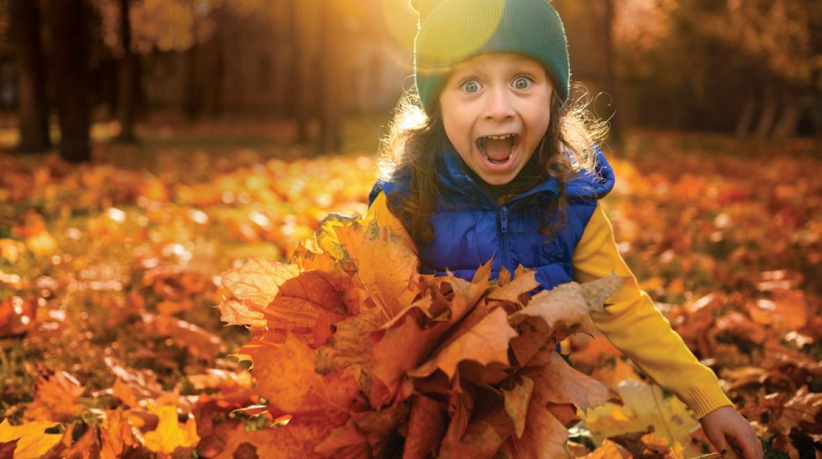 Young girl with a big smile holding a bunch of fall leaves