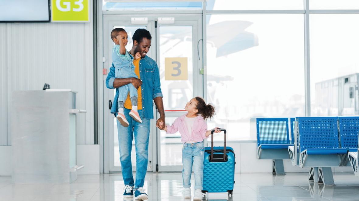 Father carrying baby and  holding hand of a young girl pulling a suitcase in an airport