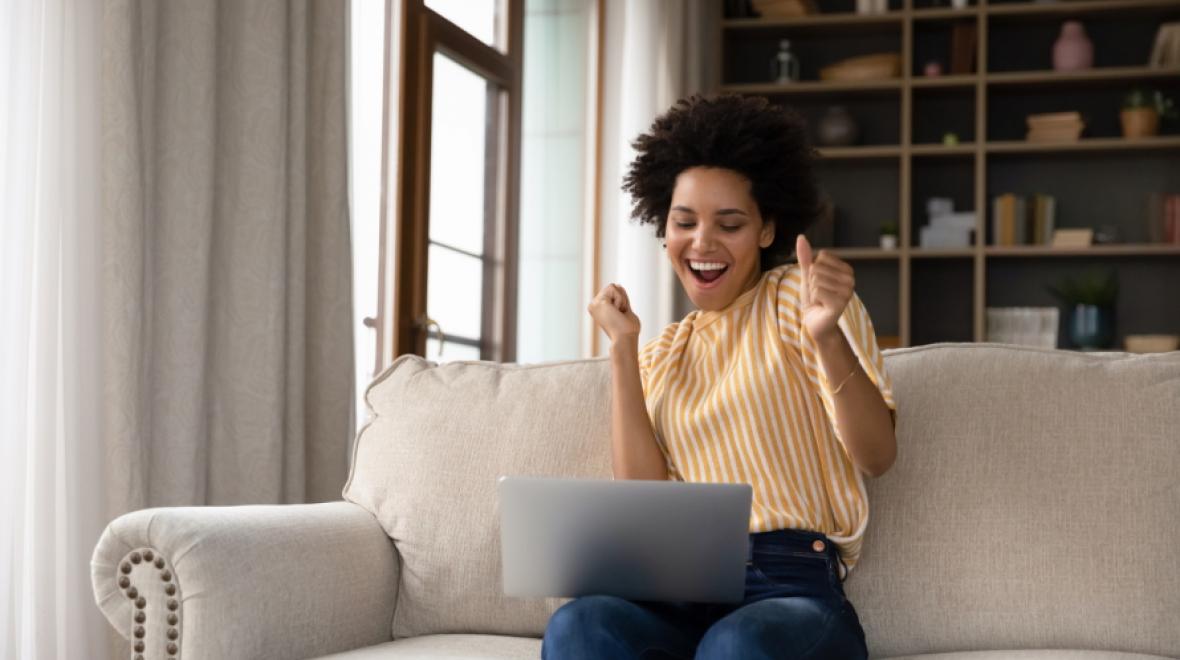 woman sitting on couch looking exciting holding a laptop