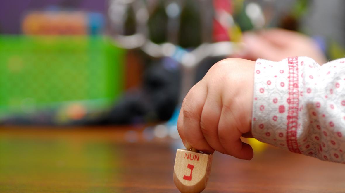 A young child's hand holds a dreidel to spin for Hanukkah - events for kids and families around Seattle celebrating Hanukkah