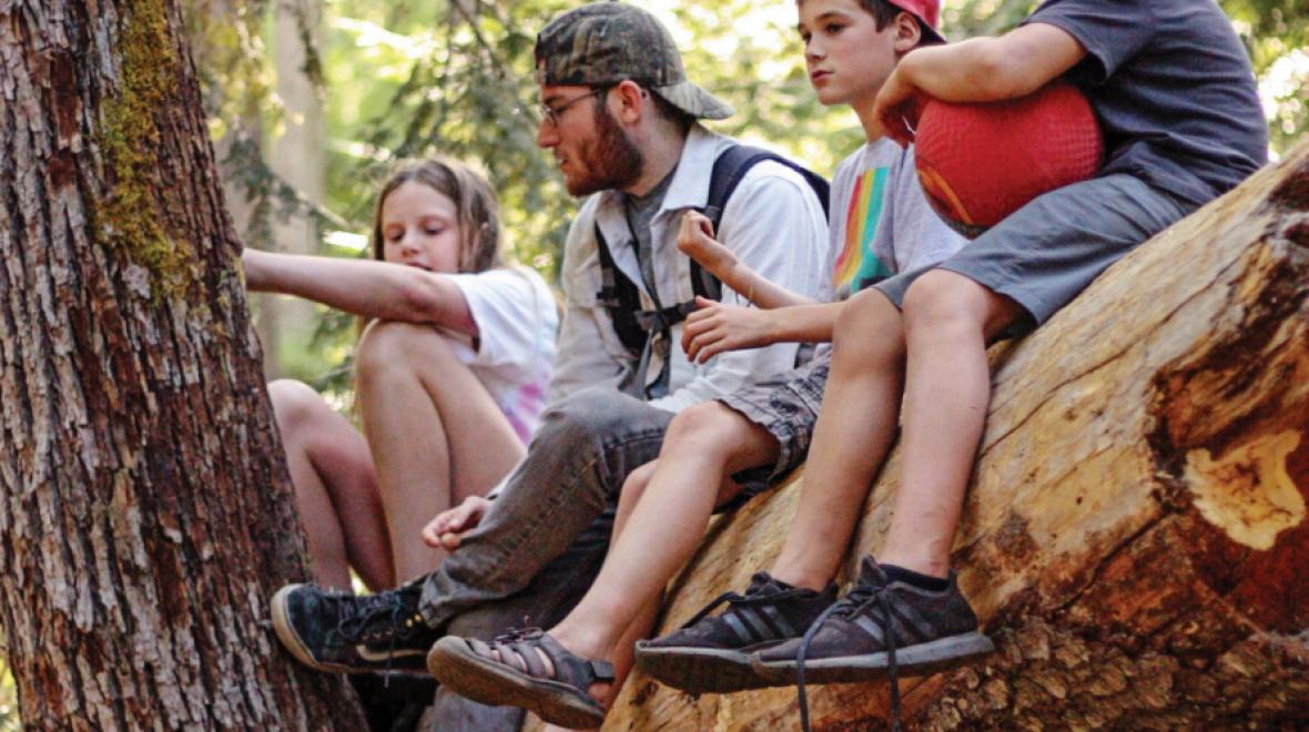 Kids sitting on a fallen tree with a camp counselor 