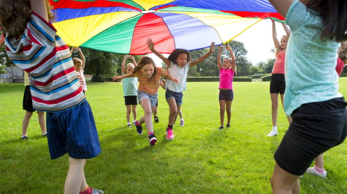 Kids holding up a parachute while two children run under it 