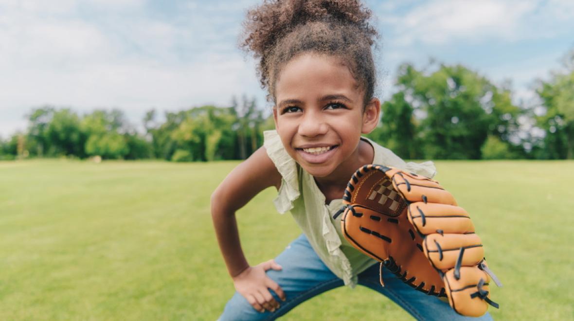 Young girl standing in a field wearing a baseball glove