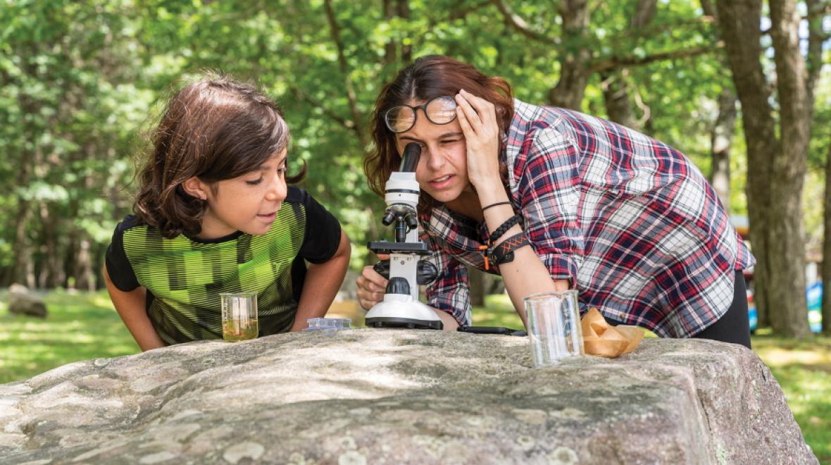 Two people looking through a microscope sitting on a large rock