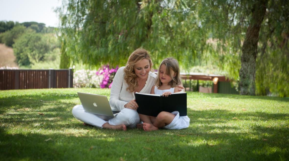 Jessica Joelle Alexander, and her daughter Sophie, sitting in the grass with a book and a computer