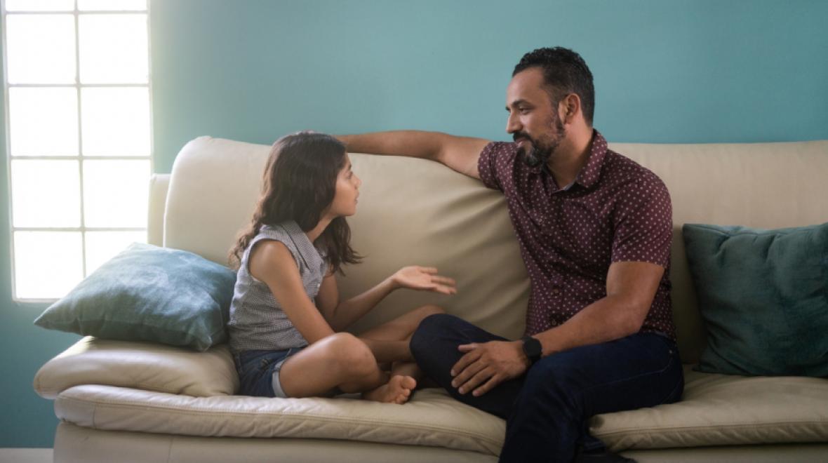 Dad and daughter sitting on a couch. The daughter is talking and dad is listening.
