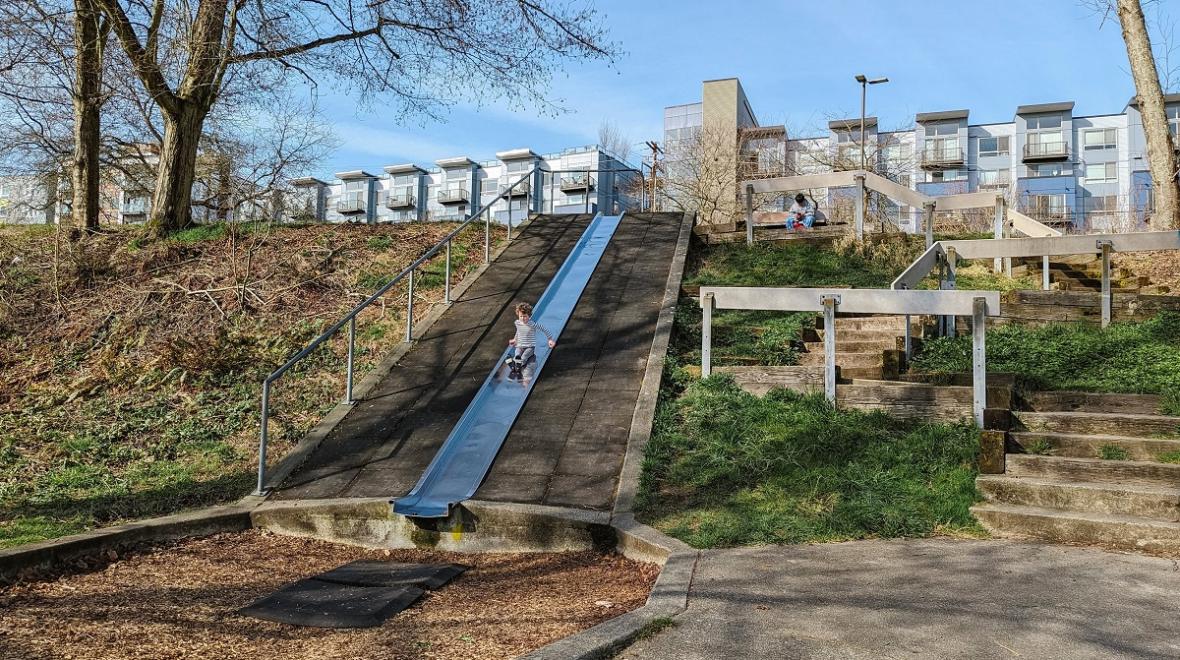 A young boy slides down a steep metal hillside slide the signature feature at South Seattle's Othello Park playground among the best for adventurous play