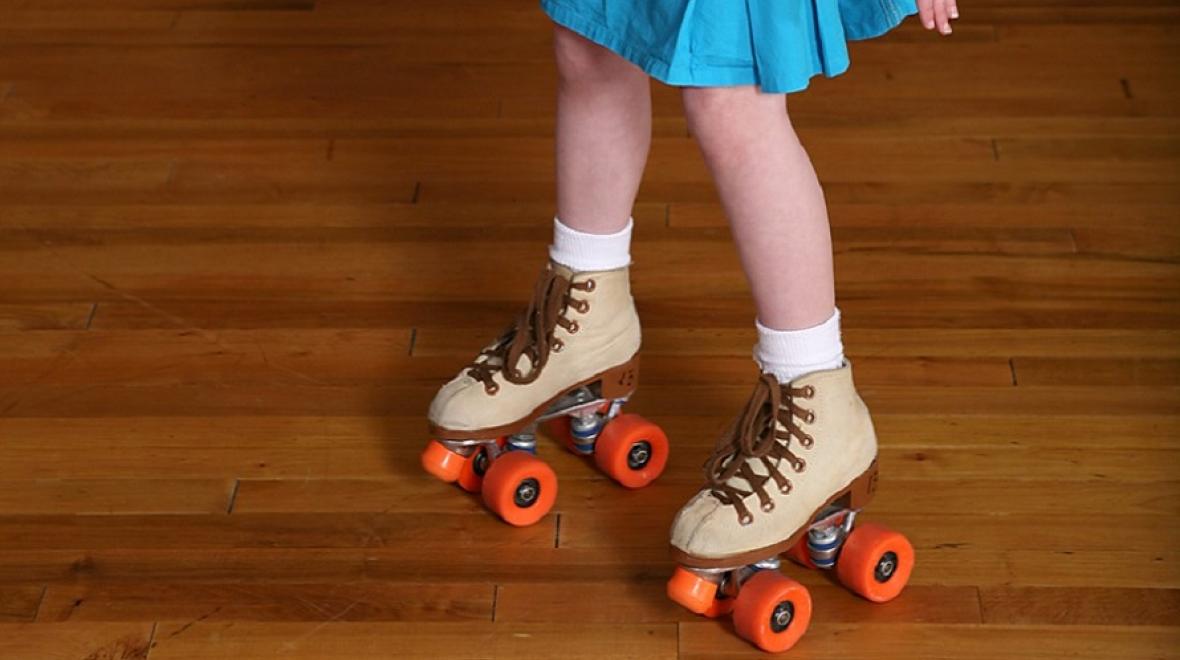 View of the legs and feet of a girl roller skating. She is wearing a blue skirt and enjoying the roller skating rink
