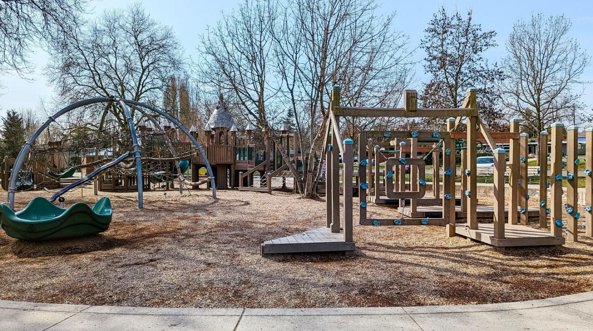 Wide view of Roxhill Park’s playground in West Seattle, including the dome climber, open climbing holds on squares and castle-themed play structure