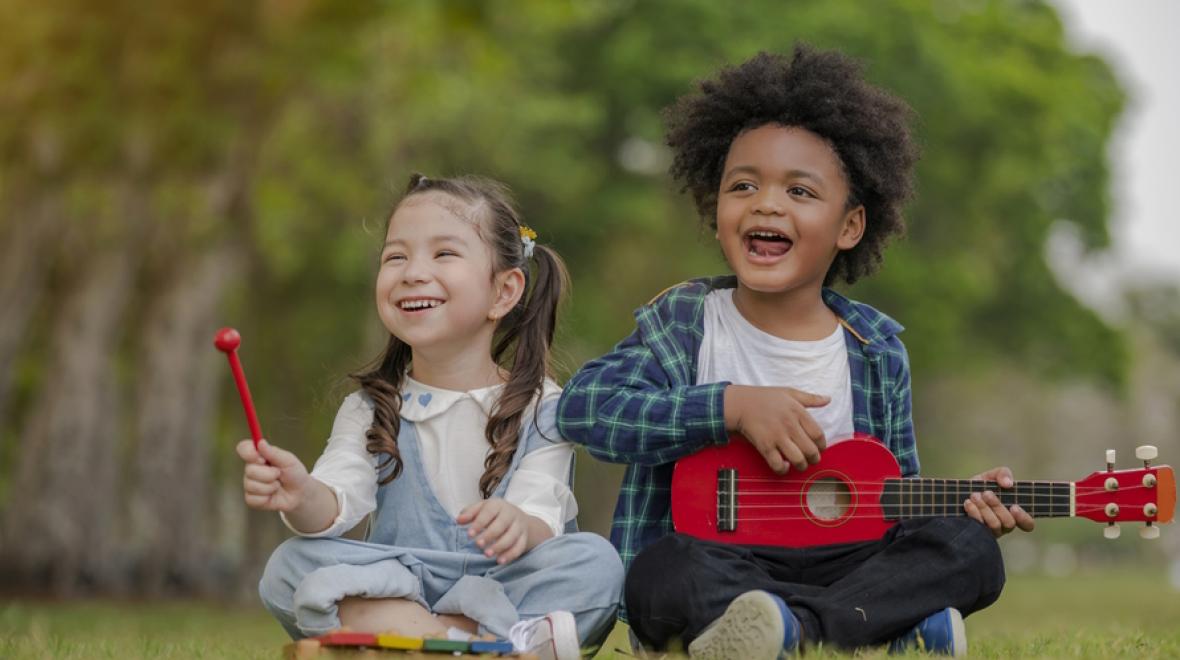 Two young children playing instruments sitting in the grass smiling