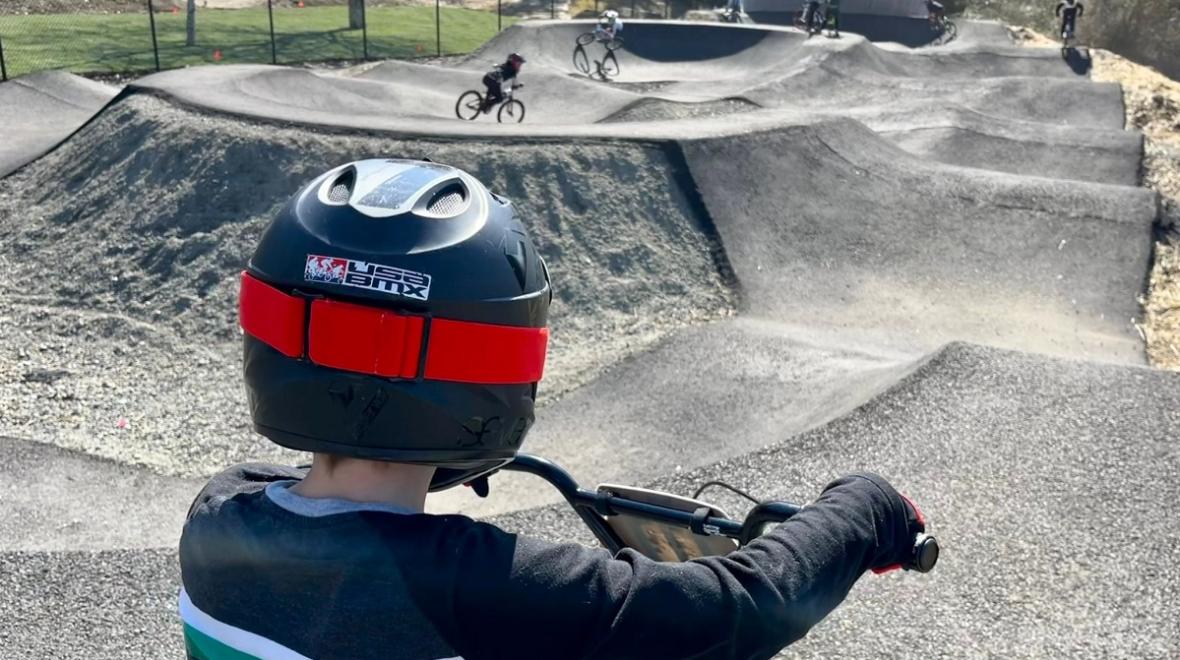 A child on a bike wearing a helmet facing away from the camera looks out over the new North SeaTac Park pump track, a paved bike course for kids on bikes