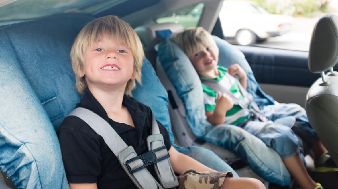 Two boys in car seat smiling in backseat of car