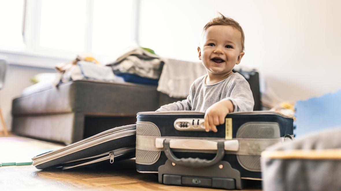 Traveling with a baby who is sitting in a suitcase and smiling