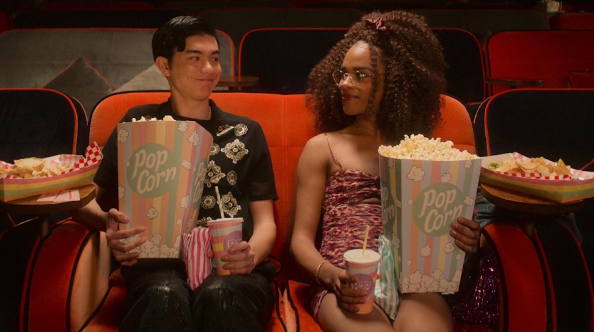 Two teens sitting in a movie theater holding popcorn and drinks. A still frame from Netflix show Heartstopper: Season 2