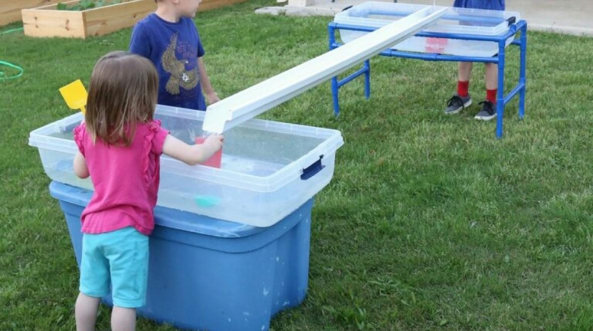 Kids playing with a piece of gutter filled with water is an easy DIY backyard water play idea