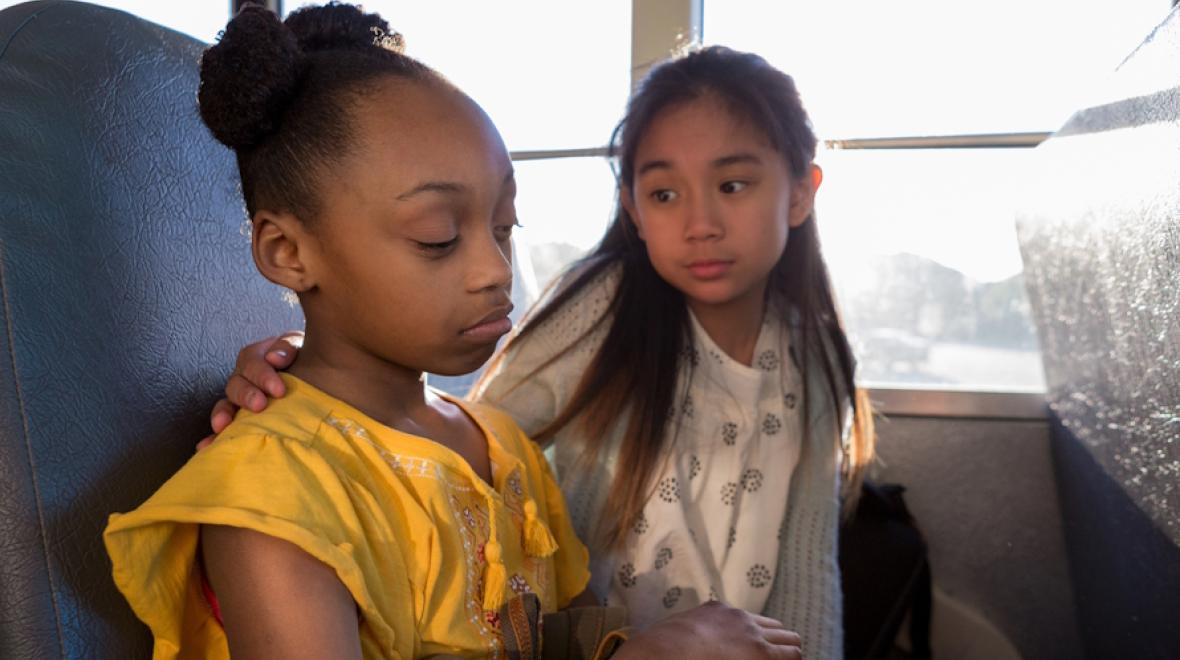 Young girl comforts her friend who looks sad on a school bus