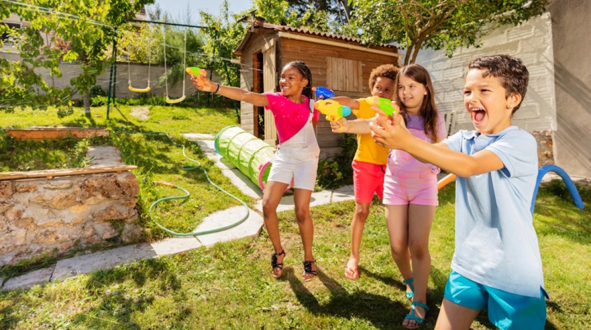 Kids shooting squirt guns at something and laughing as they play with water in the backyard