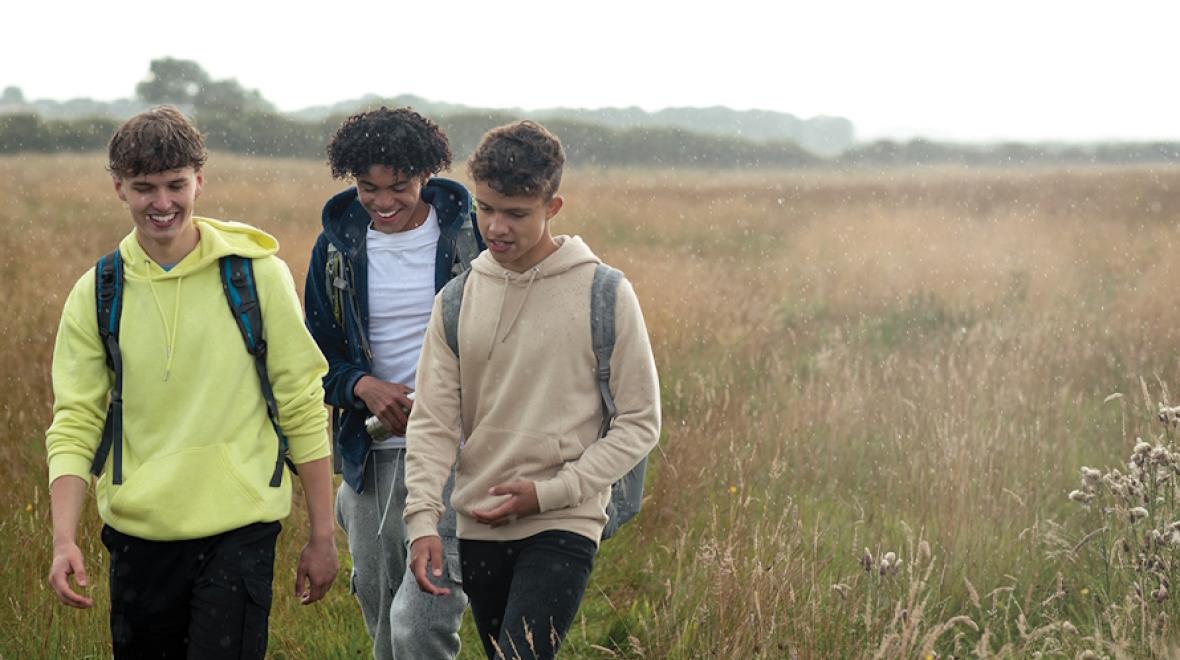 Three teenage boys walking in a field of grass 
