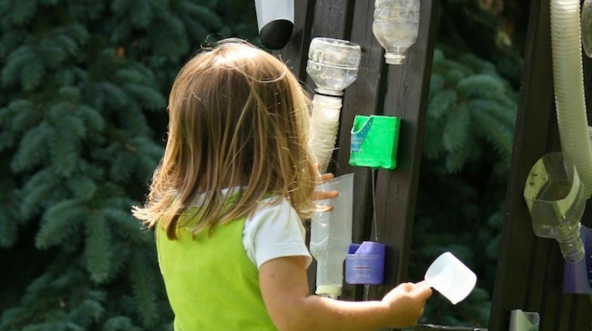 Young girl playing on a water wall made from recycled bottles is an easy backyard water play idea