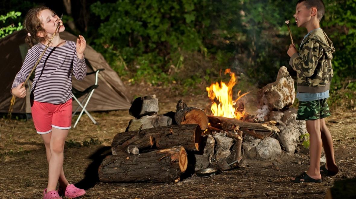 Kids eat roasted marshmallows by their campfire while camping with their family summer fun