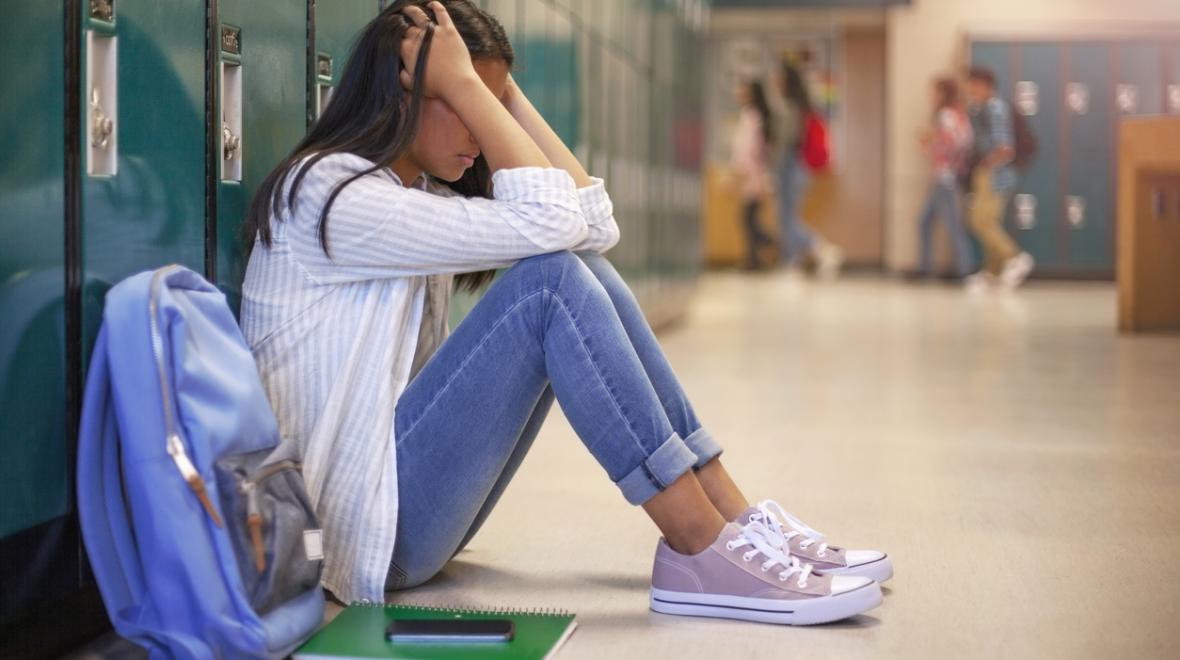 a frustrated student sits with head in hands in front of her locker, signs of toxic achievement culture