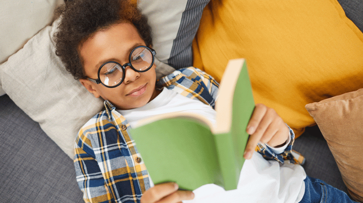 a boy with glasses reads a banned book on a pile of pillows